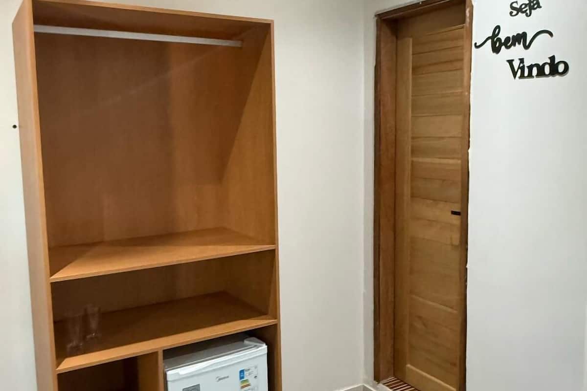 A room with a wooden wardrobe, a small white refrigerator, and a wooden door.