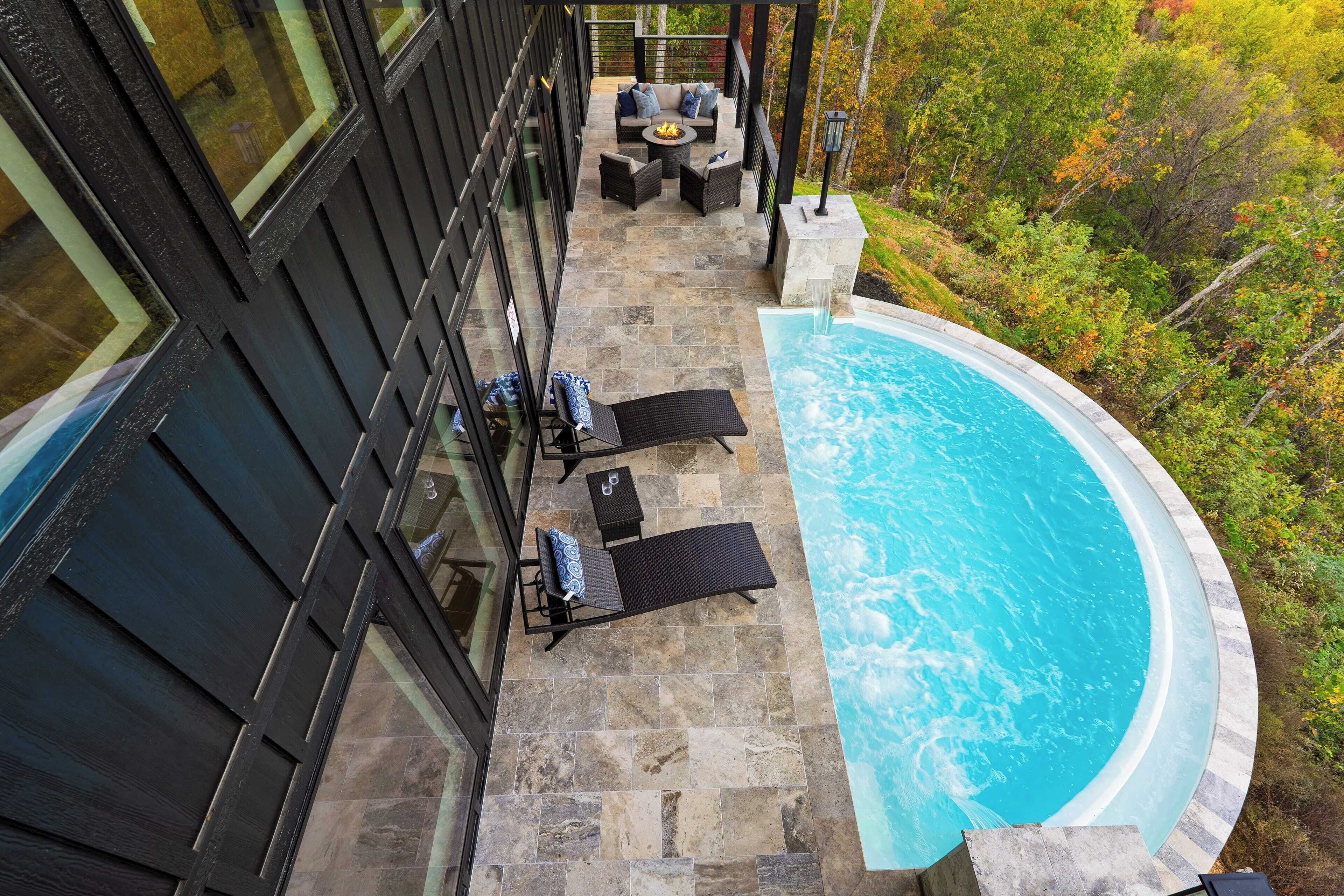 A rooftop pool area with a stone deck, lounge chairs, and a fire pit.