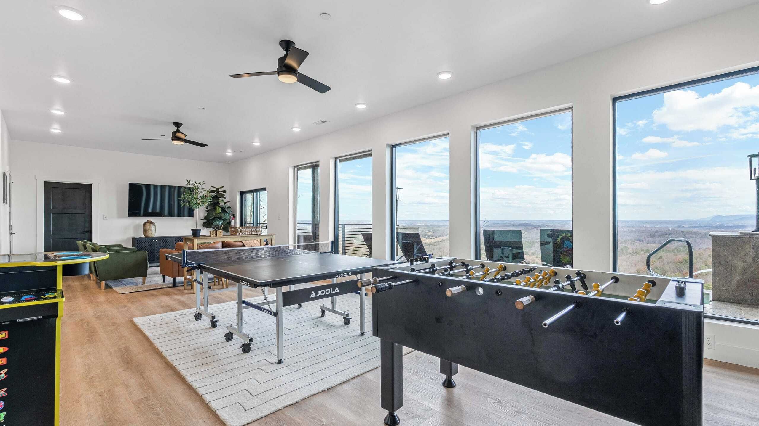 A spacious room with a ping pong table, a foosball table, and a large window offering a view of the landscape.