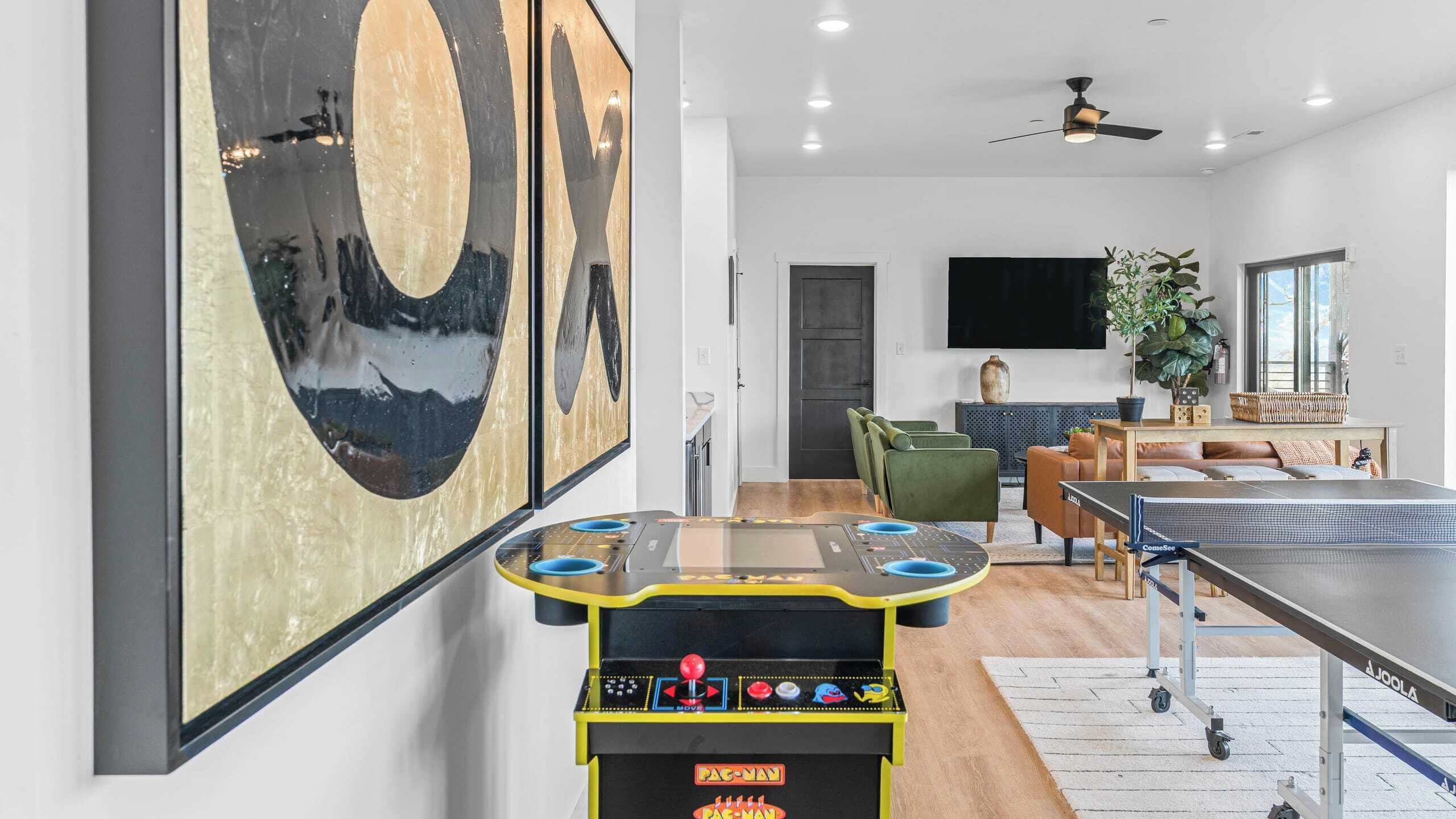 Una sala de estar moderna con una mesa de ping pong, sillas verdes y un cuadro grande en la pared.