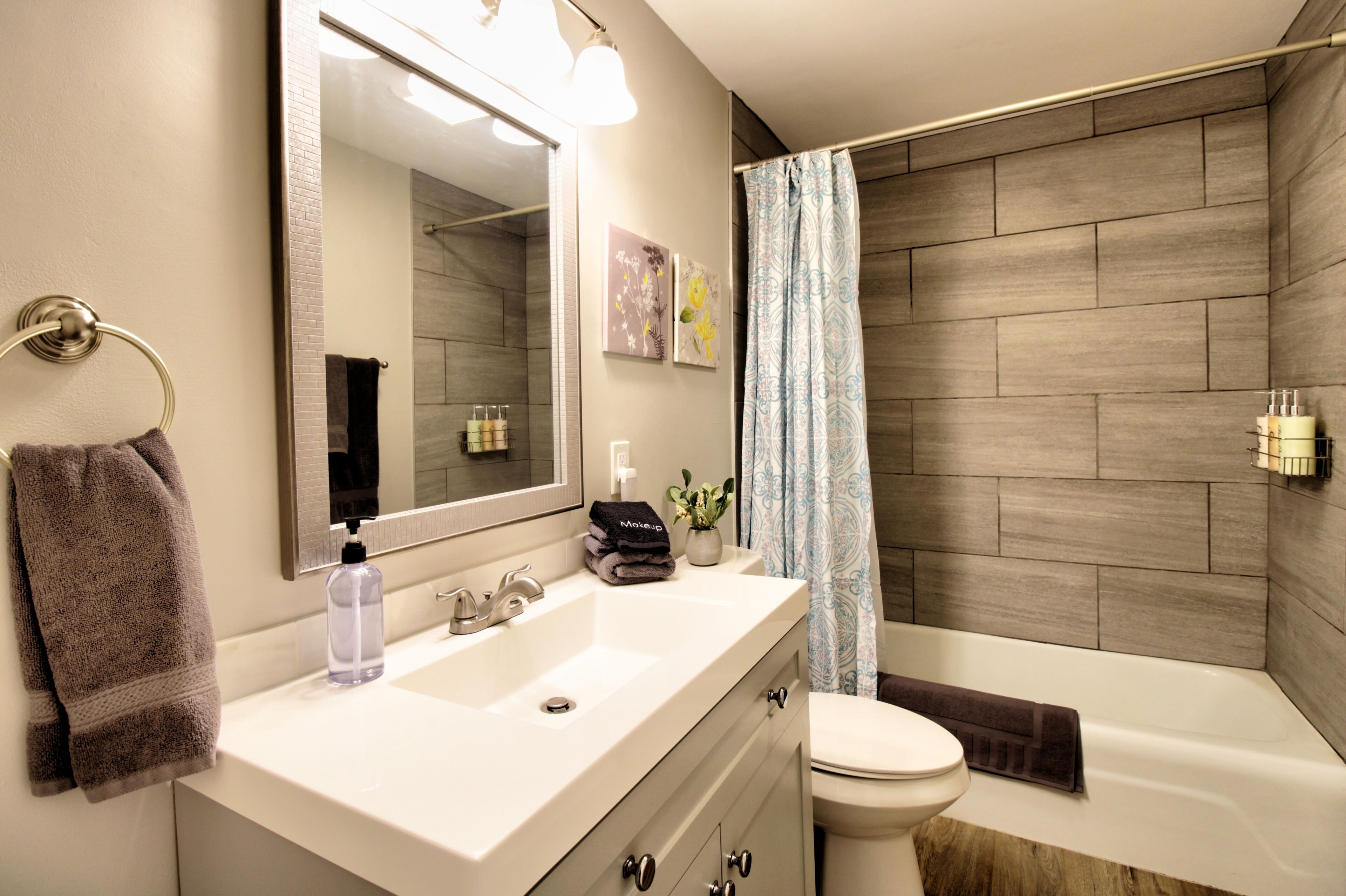 A modern bathroom with a white sink, a large mirror, a toilet, and a shower area with a patterned curtain.