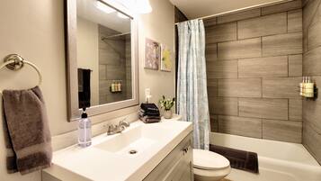 A modern bathroom with a white sink, a large mirror, a toilet, and a shower area with a patterned curtain.