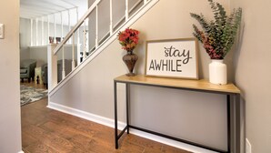 A hallway with a console table displaying a sign that says "stay awhile" and two vases with flowers. - "Broken Arrow 3-Bedroom Retreat – Cozy, Family-Friendly with WiFi & AC!" (Broken Arrow)