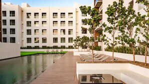 A modern building with multiple floors, a swimming pool, and a landscaped area with trees and seating.