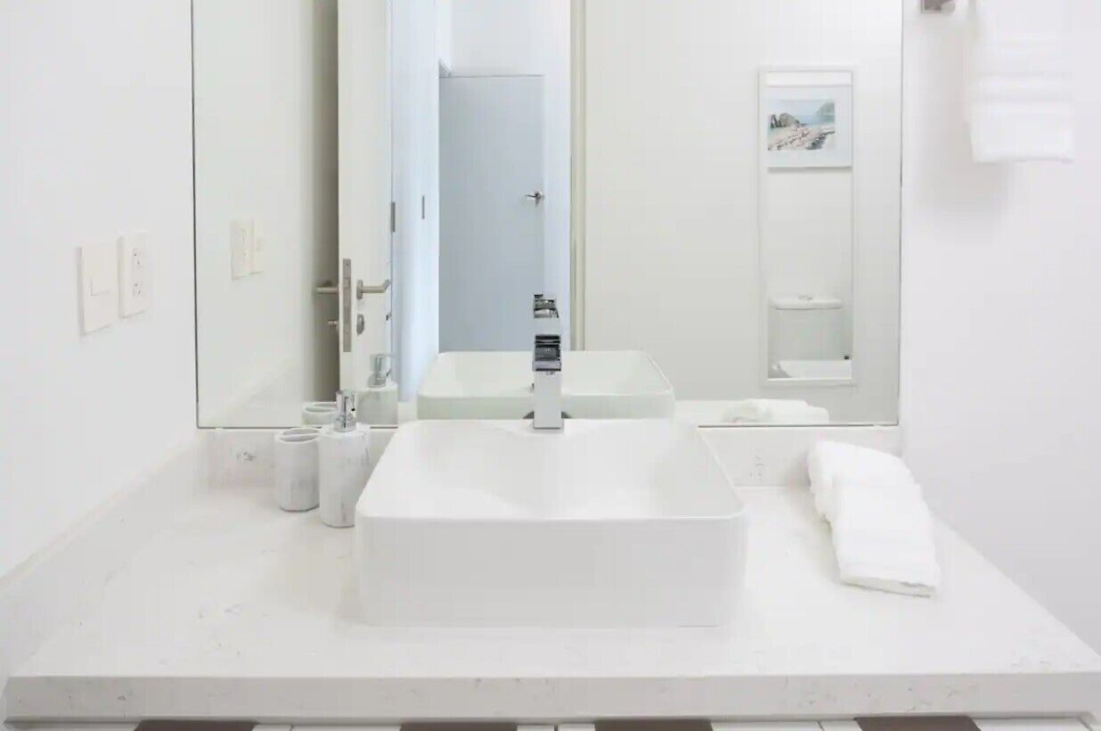 Un baño moderno con un espejo grande, un lavamanos rectangular y un inodoro.