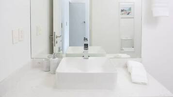Un baño moderno con un espejo grande, un lavamanos rectangular y un inodoro.