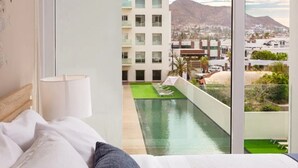 A hotel room with a large window overlooking a swimming pool and a cityscape with mountains.