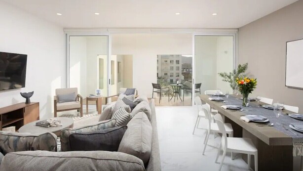 A modern living room with a sofa, coffee table, and TV, leading to a dining area with a table set for four.