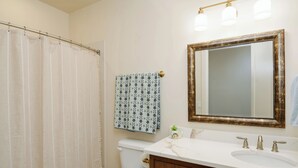 Une salle de bain avec des toilettes blanches, un rideau de douche, une serviette à motifs, un meuble-lavabo avec un miroir et un évier.