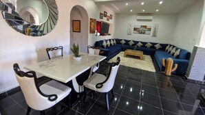 A modern living room with a dining area, featuring a spiral staircase, a blue sofa set, and a large mirror. - Villa Dar sukar  (Marrakech)