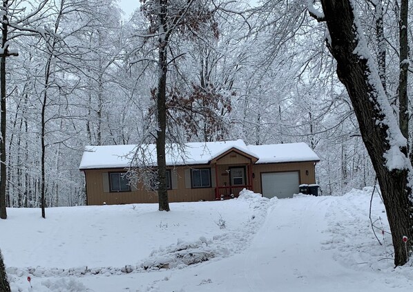 A two-story house with a snow-covered roof and a garage, surrounded by a snowy forest. - Charming 3-bedroom cabin with wonderful nature view in Farwell (Farwell)