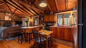Interior rústico con mesa de comedor de madera, sillas, chimenea y zona de cocina.