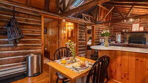 Interior de una cabaña de madera con comedor, chimenea y cocina.