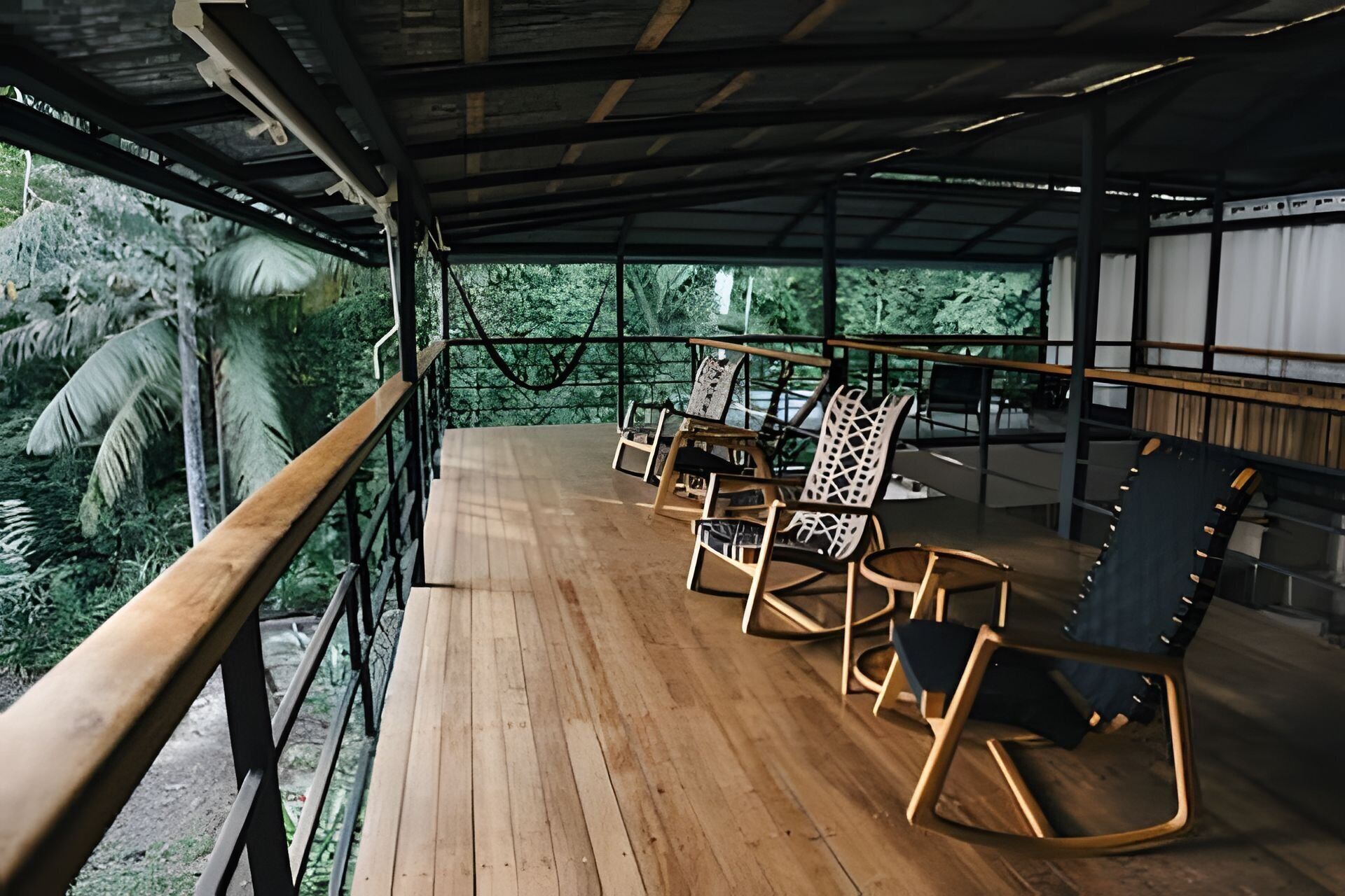 A covered wooden deck with chairs and a table, overlooking a lush green landscape.