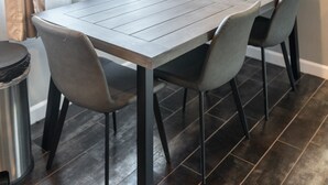 Uma mesa retangular para refeições com quatro cadeiras, soalho de madeira escura e um cesto de metal.