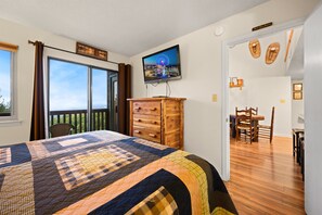 Une chambre dotée d’un grand lit, d’une commode, d’une télévision et d’un balcon offrant une vue sur le paysage urbain.