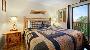 Een slaapkamer met een groot bed, twee nachtkastjes met lampen, een houten hoofdbord, een sprei en een raam met uitzicht op bomen.