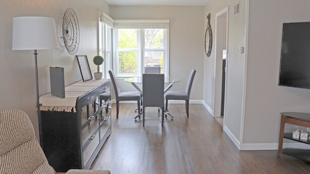 A modern living room with a glass dining table, grey chairs, a sofa, a lamp, and a TV.