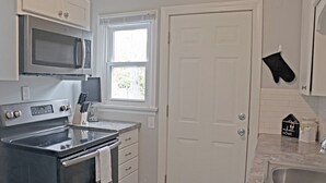 A kitchen with a stainless steel stove, microwave, and oven, white cabinetry, a window, and a door.