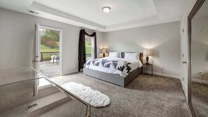 Ein Schlafzimmer mit Bett, Nachttischlampen, einem Glastisch, einem flauschigen weißen Teppich und Blick ins Freie.