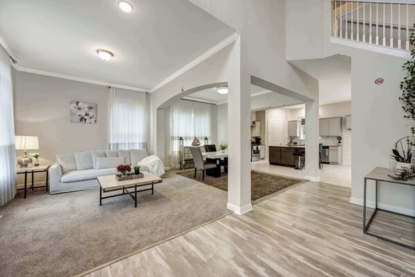 A spacious living area with a sofa, coffee table, and a dining table with chairs. There is a kitchen area visible in the background.