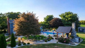 Ein Garten mit Schwimmbecken, Liegestühlen, einem Pavillon und einem Kamin aus Stein.