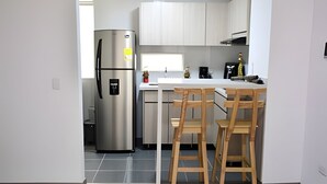 A modern kitchen with white cabinets, a stainless steel refrigerator, a small island with bar stools, and a window providing natural light. - Spectacular Apartment in the Zona Rosa - Stratum 5 (Manizales)