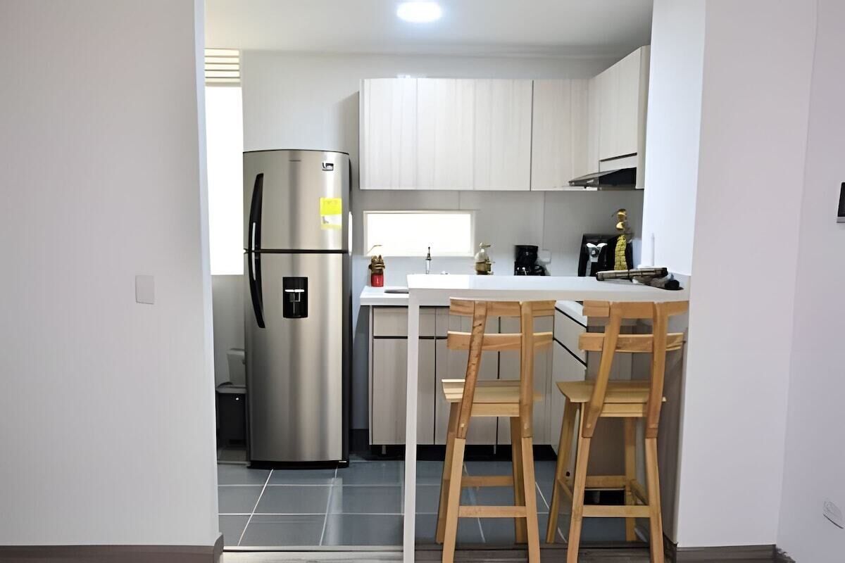 Eine kleine Küche mit einem Edelstahl-Kühlschrank, einer weißen Arbeitsplatte und zwei hölzernen Barhocker.