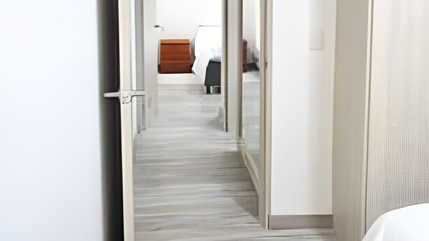 A hotel hallway with a wooden floor, a bed with a white bedspread, and a wardrobe with a mirror. - Spectacular Apartment in the Zona Rosa - Stratum 5 (Manizales)