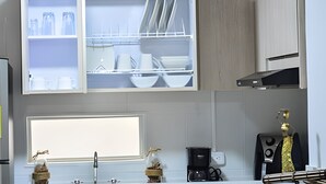 A modern kitchen with open cabinets displaying dishes and utensils, a coffee maker, and a decorative plant. - Spectacular Apartment in the Zona Rosa - Stratum 5 (Manizales)