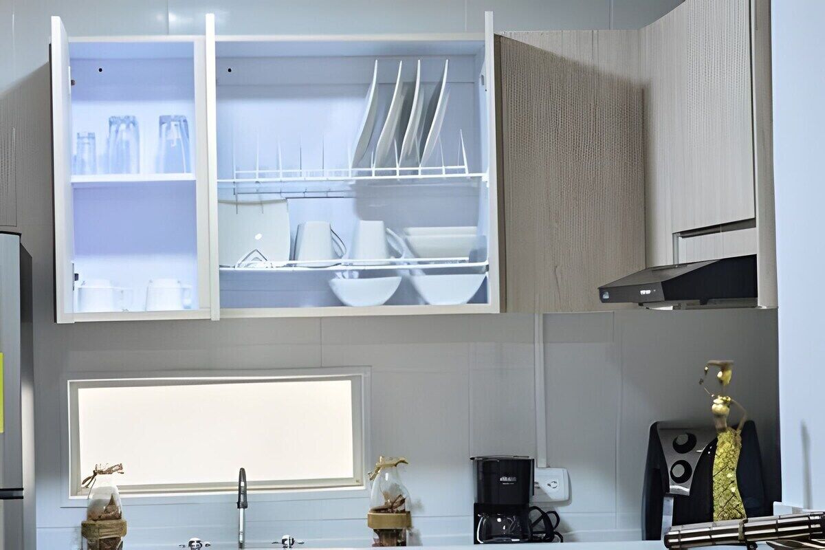 A kitchen with open cabinets displaying dishes and utensils, a coffee maker, and a decorative item on the counter.