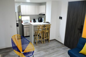 A compact kitchen with a refrigerator, stove, and wooden chairs.