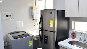 Une cuisine compacte équipée d’un réfrigérateur en acier inoxydable, d’un four encastré, d’un évier et d’une fenêtre avec des stores.
