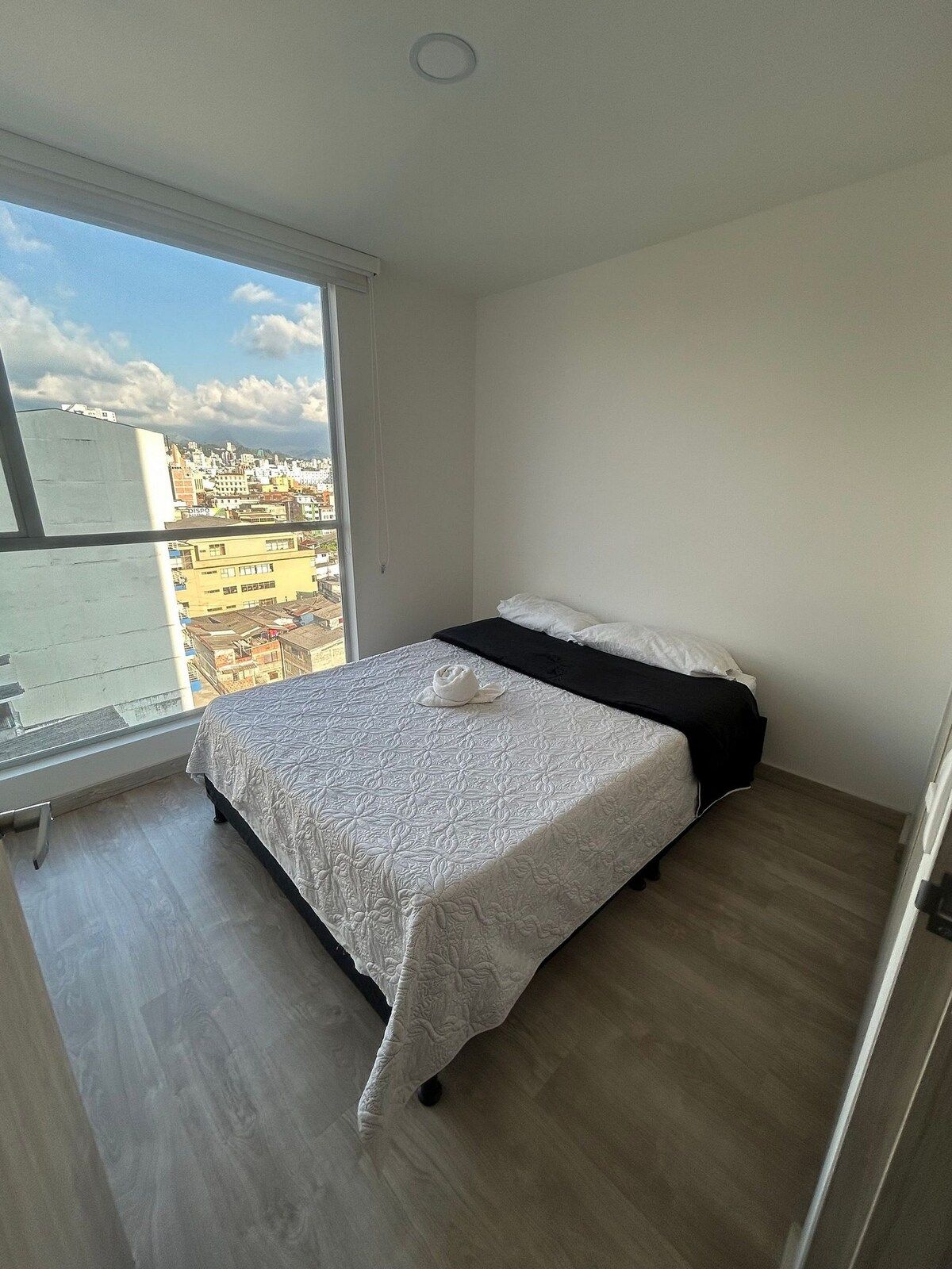 Un dormitorio con un ventanal grande, una cama y vistas a un paisaje urbano.