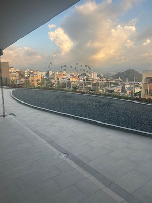 A rooftop terrace with a view of a cityscape, including buildings and palm trees.