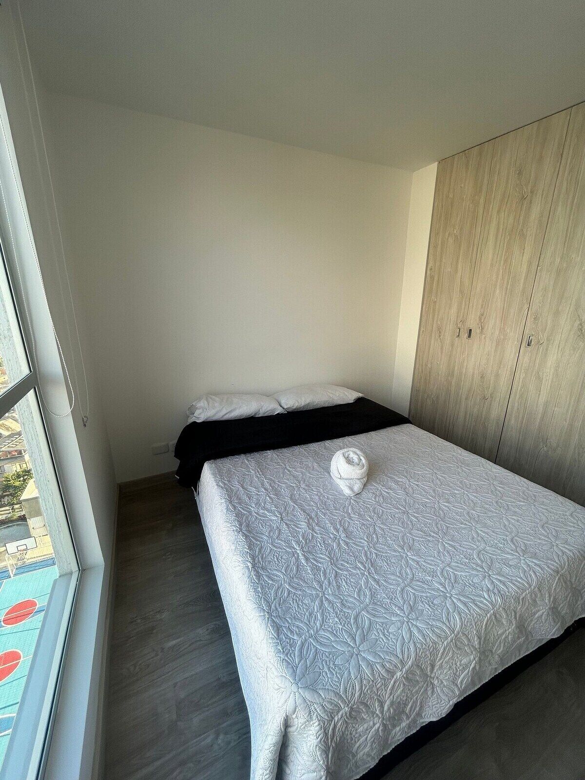 A single bed with a white quilt, a wooden wardrobe, and a window with a view of a pool.