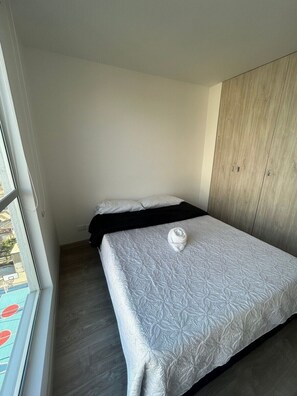 A single bed with a white quilt, a wooden wardrobe, and a window with a view of a pool. - Spacious and Luxurious -Stratum 6 (Manizales)