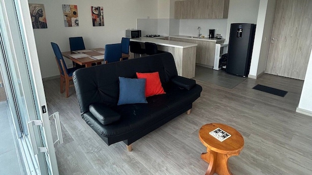 A modern living room with a black sofa, a wooden coffee table, and a kitchen in the background. - Spacious and Luxurious -Stratum 6 (Manizales)