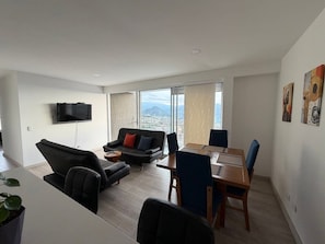A modern living room with a sofa, a dining table, and a TV mounted on the wall.