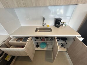 Une cuisine compacte dotée d’un évier encastré, d’une machine à café et de placards de rangement.