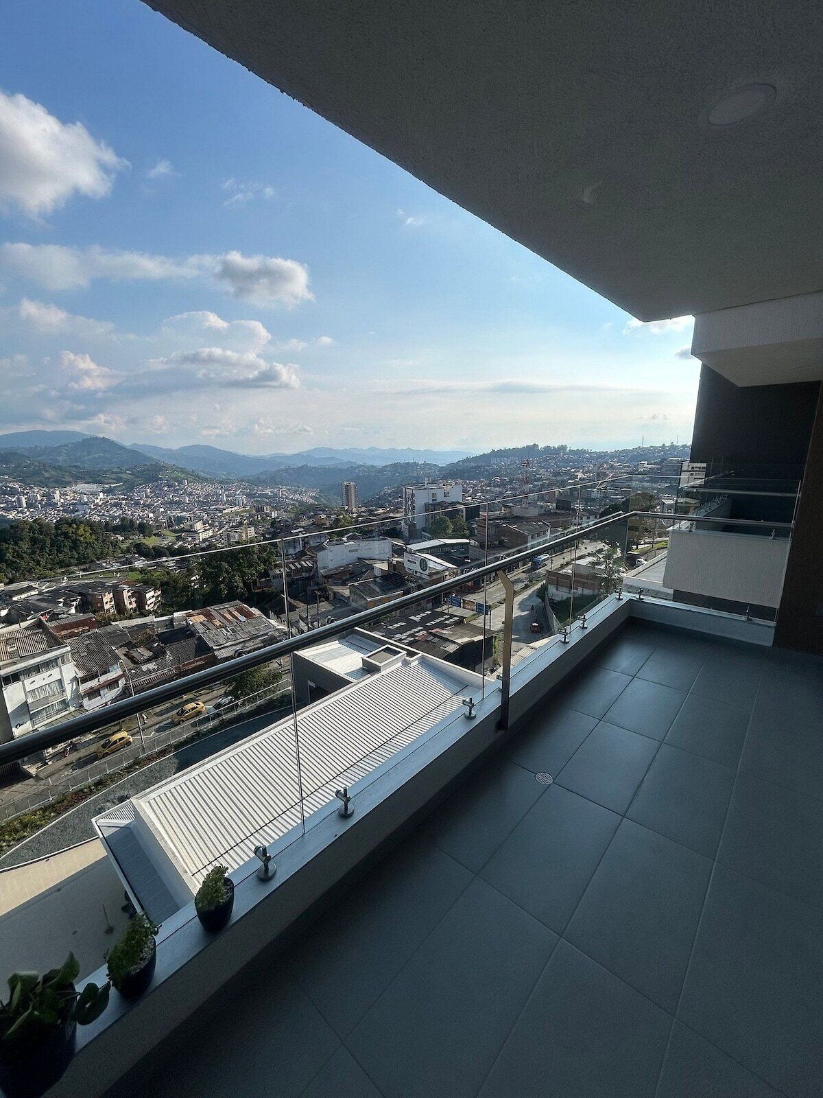 Un balcón con vista a la ciudad, que incluye edificios y montañas lejanas.