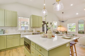 Une cuisine avec des meubles de couleur verte, un îlot central blanc et des luminaires suspendus.