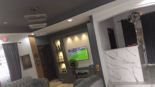 Un salon moderne avec un grand téléviseur, des canapés gris et un mur décoratif en marbre.
