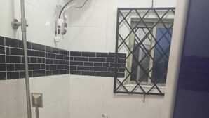 Une petite salle de bain comprenant des toilettes, une douche et une fenêtre avec une grille en métal.