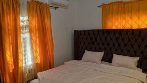 Une chambre avec un grand lit, deux oreillers et des rideaux orange.