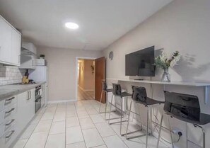 A modern kitchen with white cabinets, a flat-screen TV, and a bar area with stools.