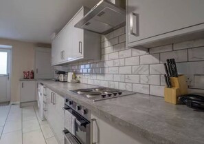 A kitchen with a built-in oven, a stovetop, and a microwave. There is a knife block on the countertop.