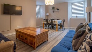 Una sala de estar con una mesa de centro de madera, un sofá azul y un comedor con una mesa y sillas.