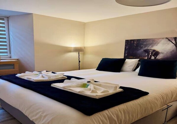 A hotel room with a large bed, two pillows, a bedside table, a lamp, and a painting on the wall.