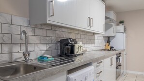 Una cocina moderna con armarios blancos, un lavamanos de acero inoxidable, una cafetera y una lavadora integrada.